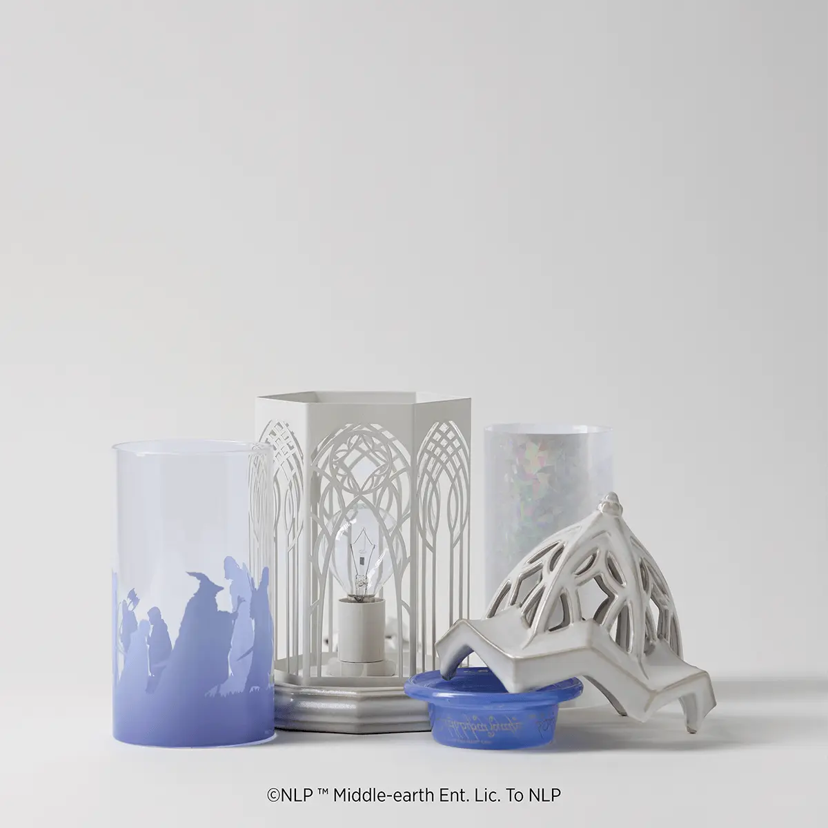 White metal Scentsy Warmer with ornate arched cutout design inspired by Rivendell architecture, displayed with coordinating blue wax melt and decorative white mountain-shaped accessory
