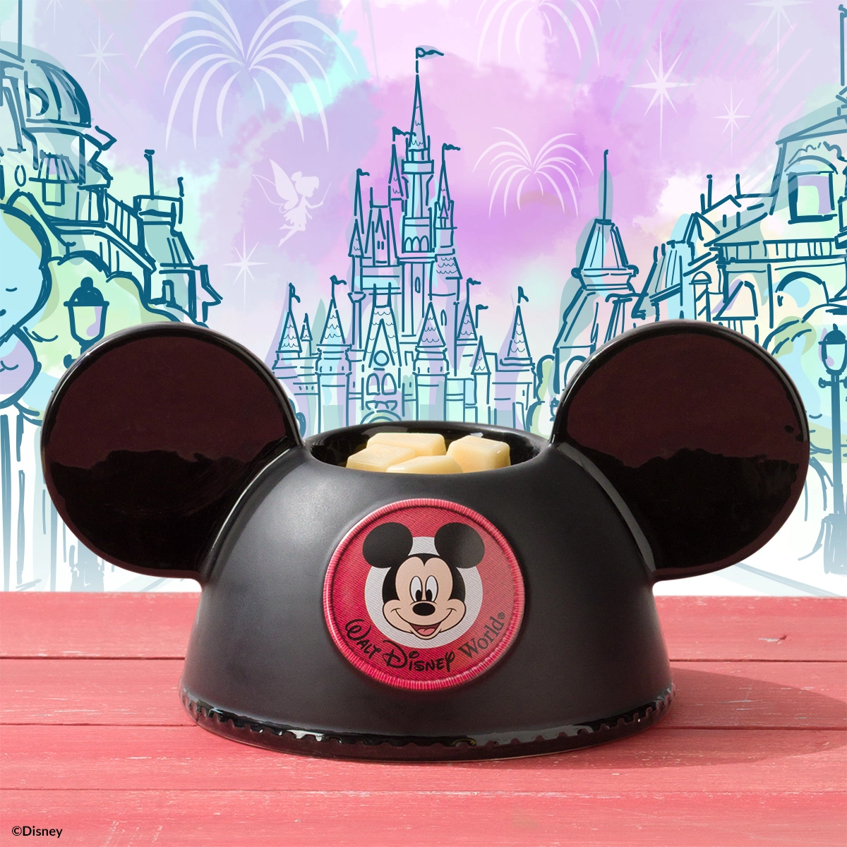 Black dome warmer shaped like Mickey Mouse's head with large round ears, embroidered Mickey face badge on front, holding cream-coloured wax, displayed against a fairytale castle backdrop