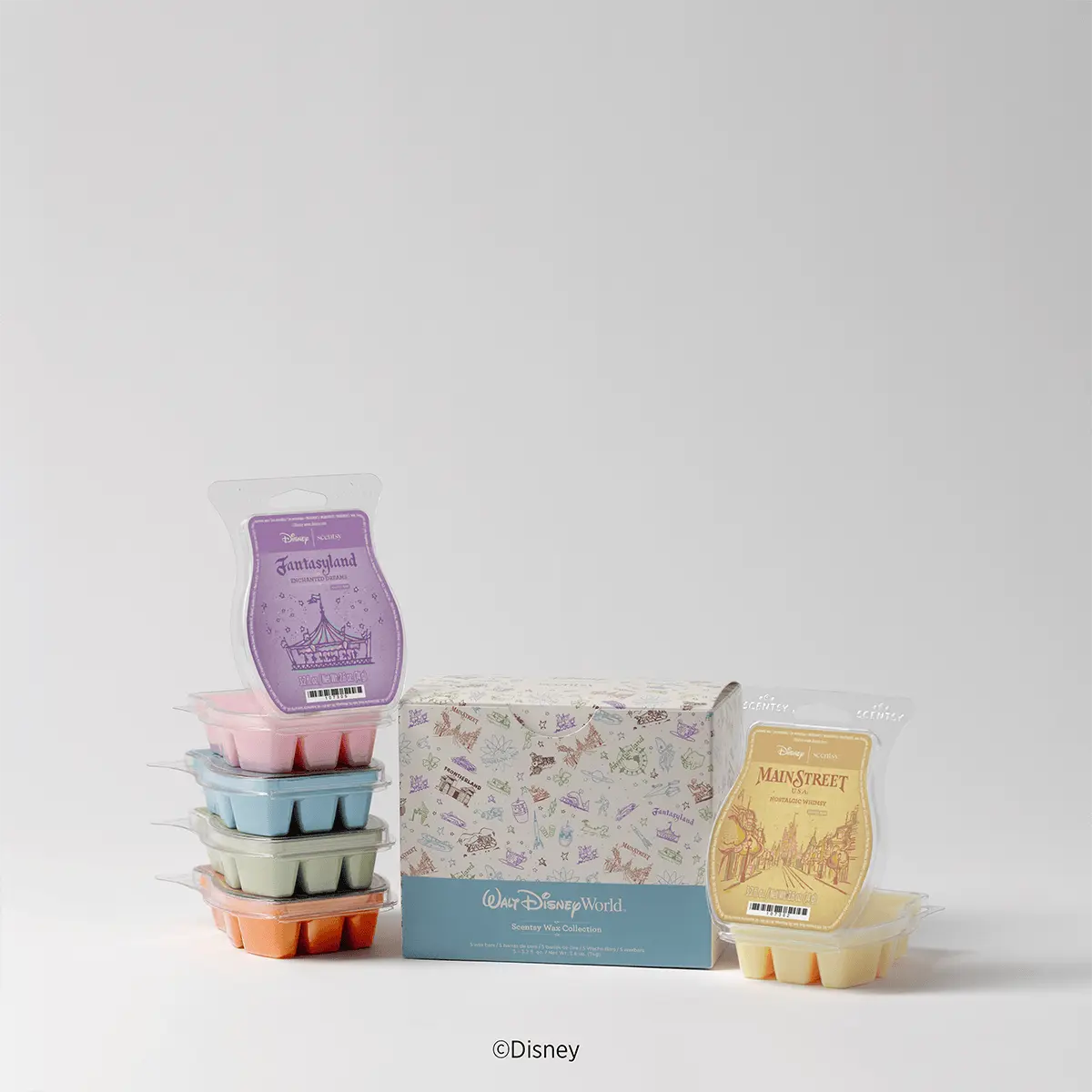 Stacked Scentsy wax bars in pink, blue, cream, and orange, a Fantasyland-themed purple wax bar with carousel packaging, a Main Street boxed wax bar in cream, and a Walt Disney World - Scentsy Wax Collection display box