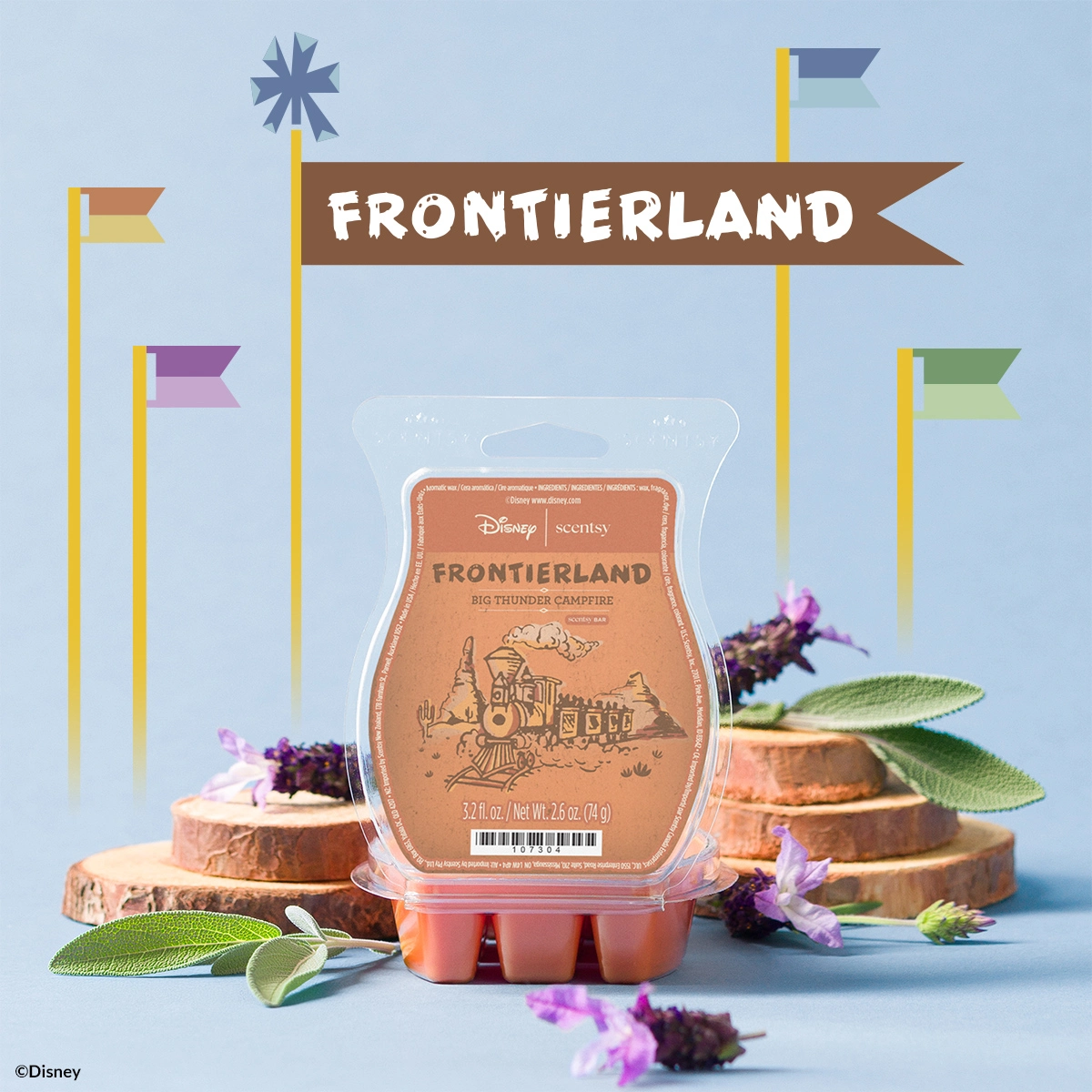 Scentsy wax bar in terracotta-coloured clamshell packaging labelled Frontierland Big Thunder Campfire, surrounded by wooden log slices, green sage leaves, and purple flowers, against a light blue background with illustrated flags and a banner