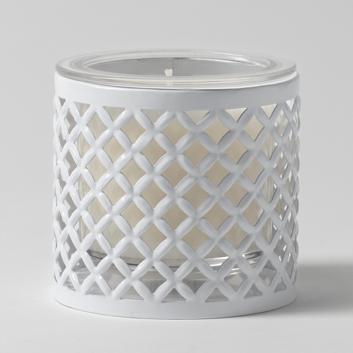 White cylindrical metal candle holder with an open lattice trellis cut-out pattern, containing a clear glass insert filled with cream wax, the White Trellis Candle Holder