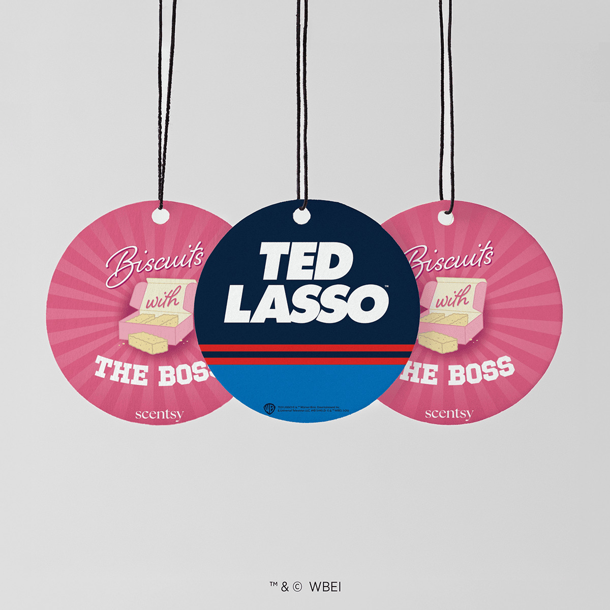 Three hanging round cards on black cords, two pink with a biscuit box design and one navy and blue Ted Lasso card, the Biscuits with the Boss Scent Circle 3-pack