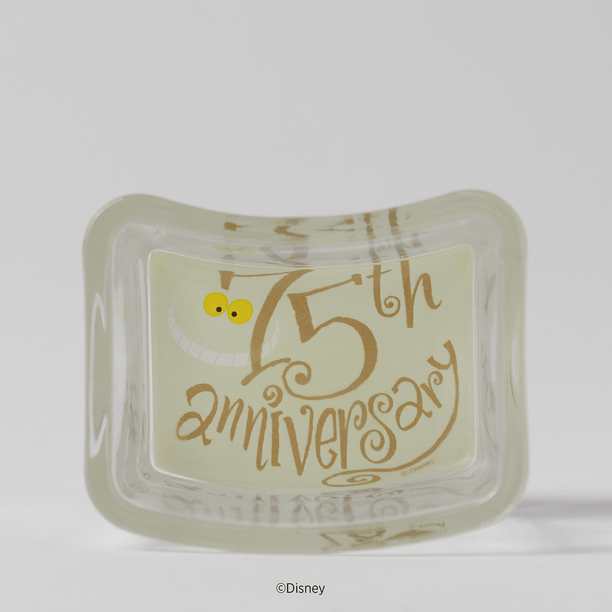 Frosted glass warmer dish with a faint Cheshire Cat grin, yellow eyes and swirling gold 75th anniversary lettering