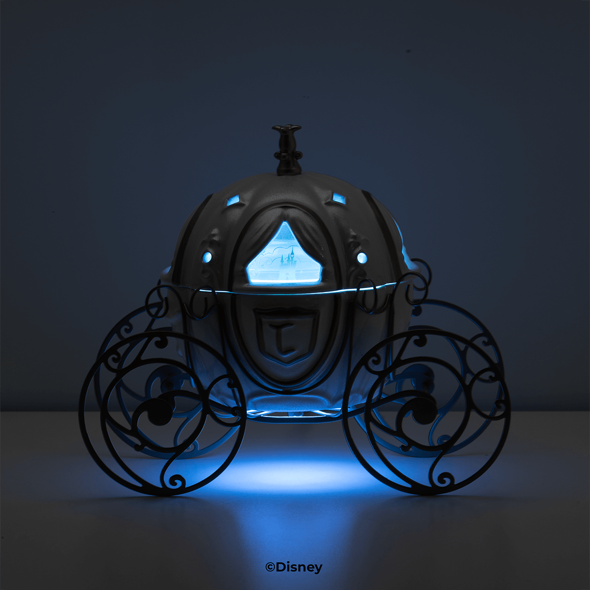 Pumpkin-shaped carriage warmer with swirling metal wheels and a castle scene window glowing blue in a darkened room