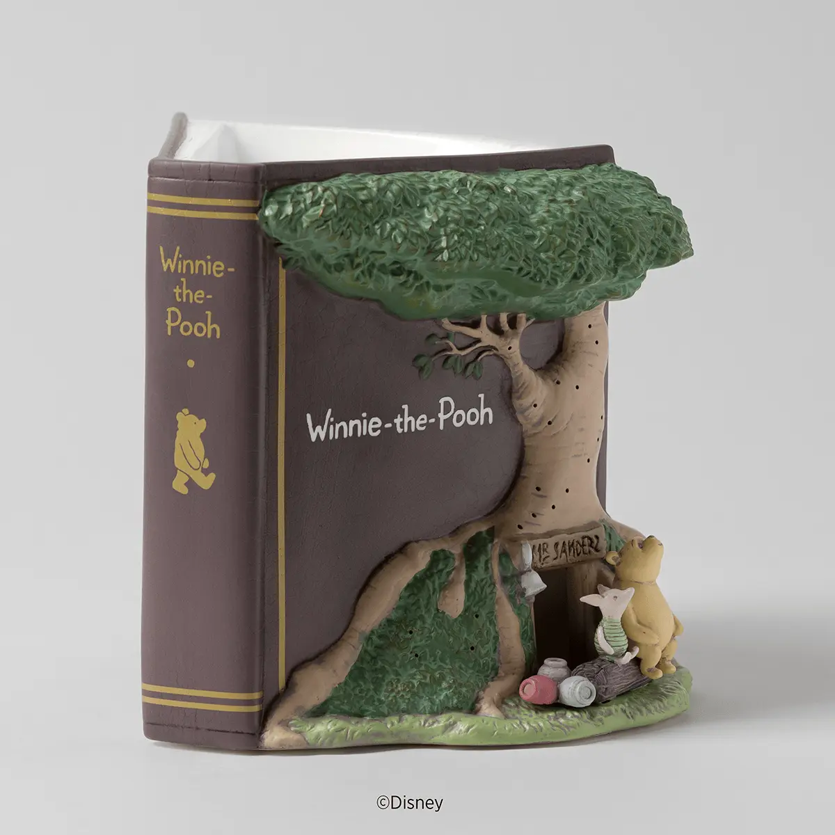 Brown ceramic storybook-shaped warmer with a sculpted tree, Winnie the Pooh and Piglet at Mr Sanders' door, and scattered honey pots