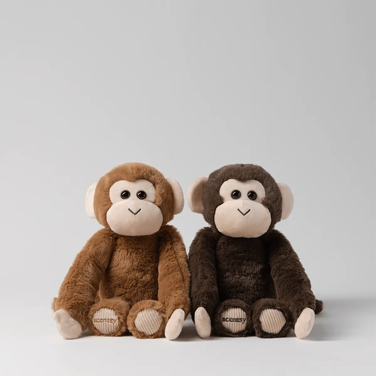 Two plush monkeys, one caramel brown and one dark chocolate brown, with cream faces, ears and hands and ribbed foot pads