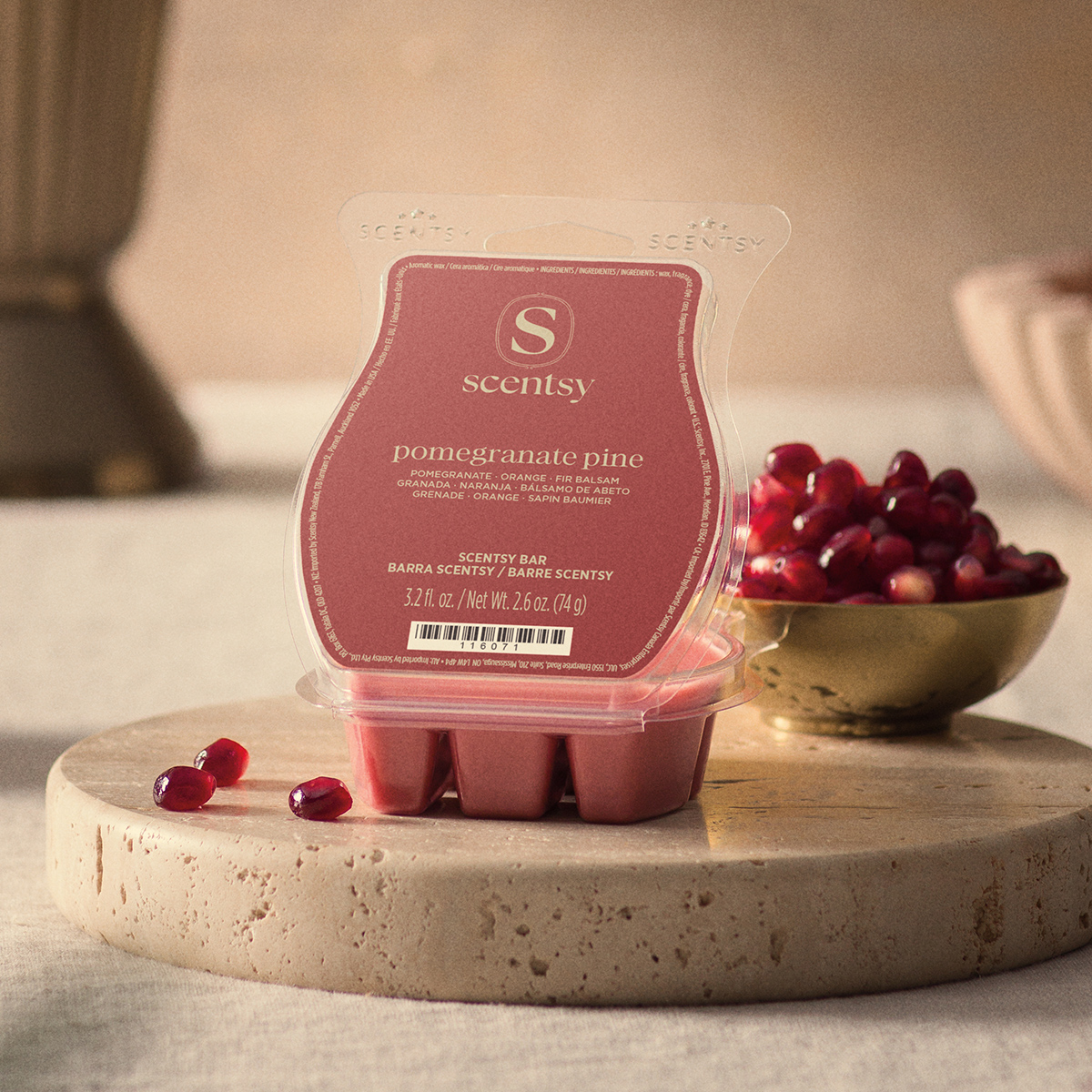 Red Pomegranate Pine Scentsy Bar in clear packaging on a travertine stone tray beside a gold bowl of pomegranate seeds