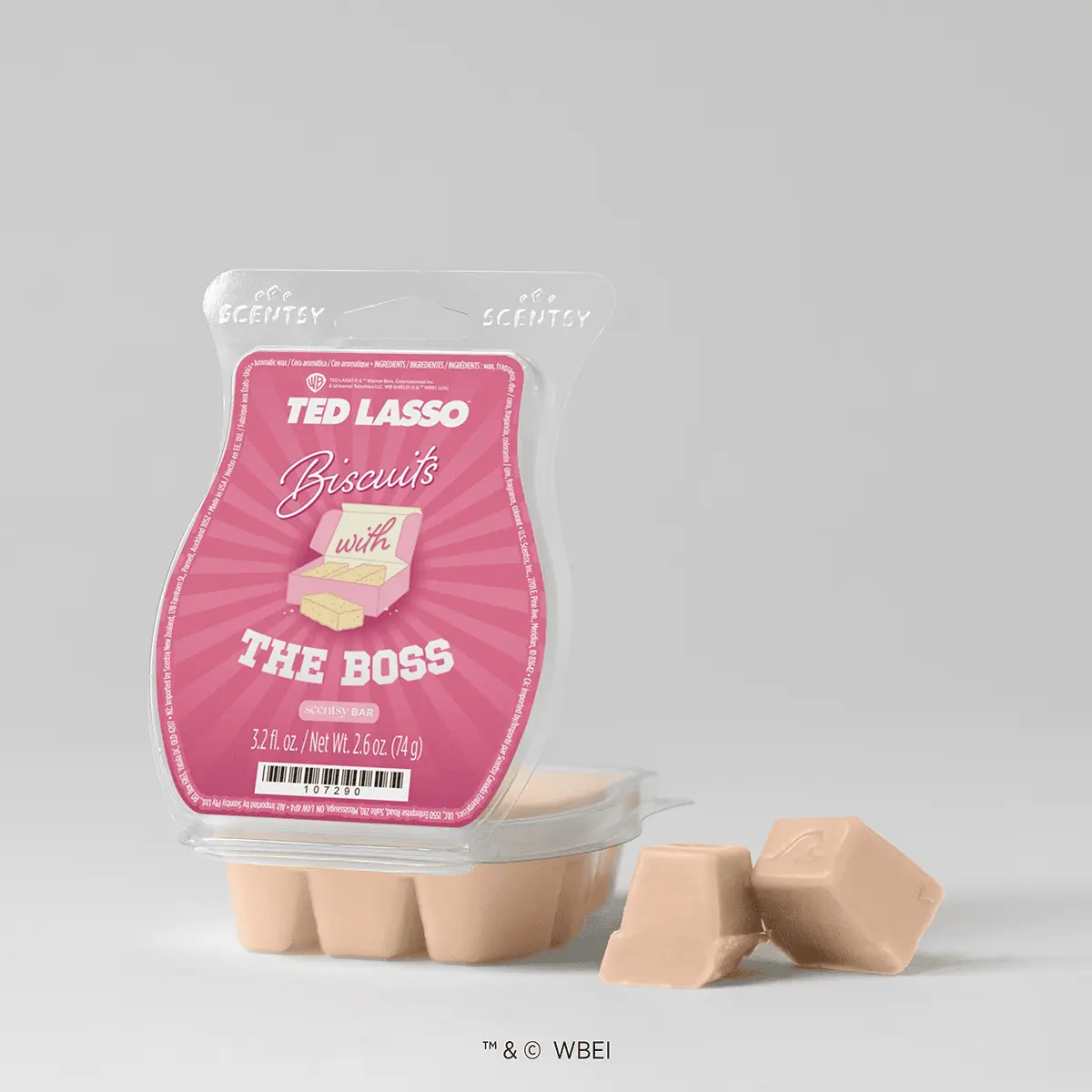 Pink Ted Lasso Biscuits with the Boss Scentsy Bar in clear clamshell packaging with a cartoon biscuit box, beside two beige wax cubes