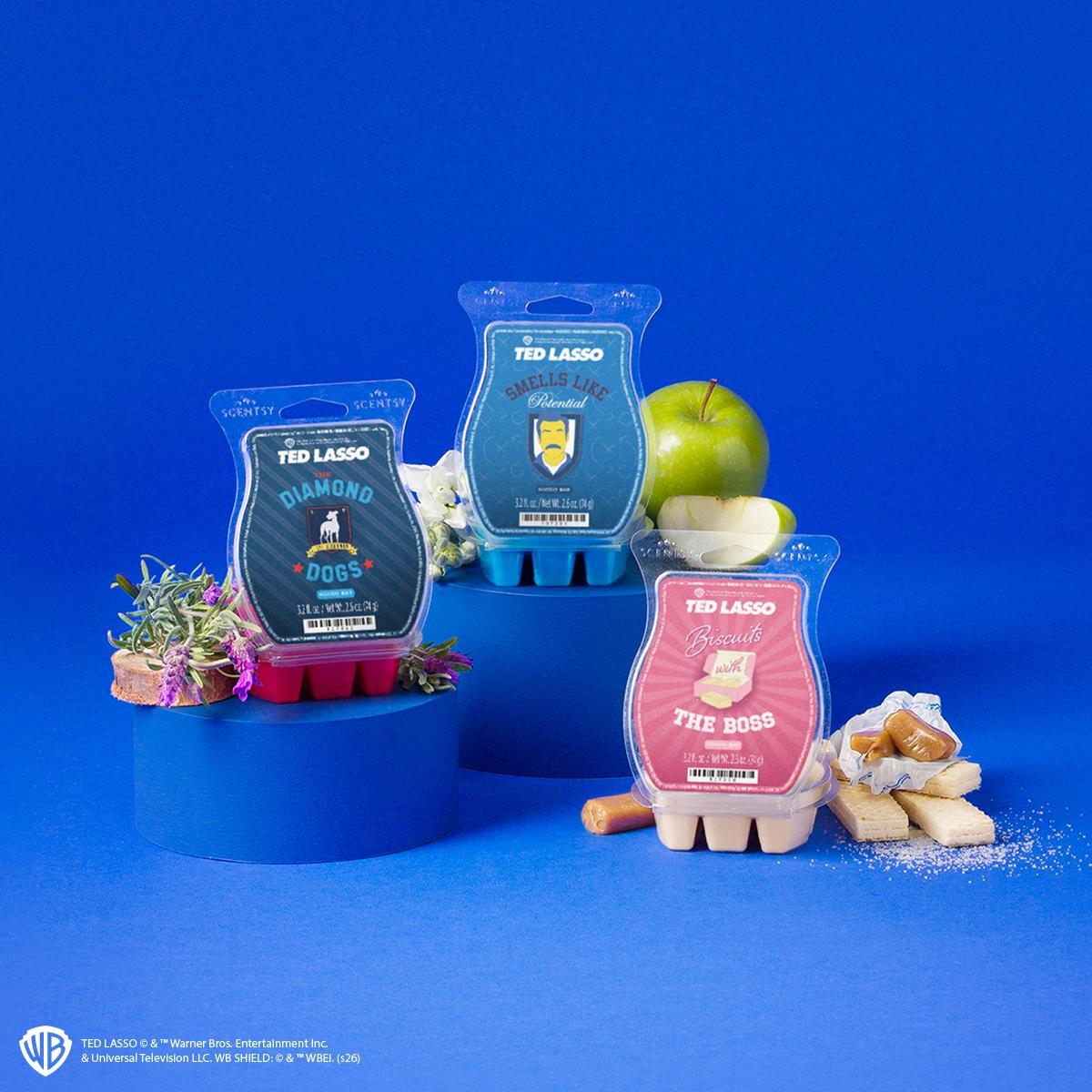 Three Ted Lasso Scentsy Wax bars in red, blue and cream on blue pedestals with lavender, green apple and shortbread, the Ted Lasso Scentsy Wax Collection